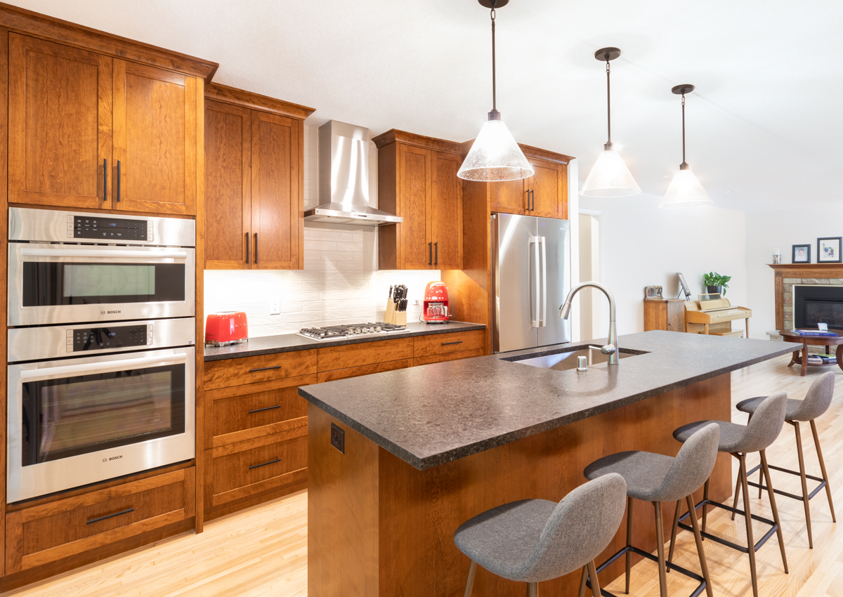 Contemporary kitchen with medium wood cabinets, a large island with a dark countertop and double wall ovens, part of a remodel in Minnetonka, MN.