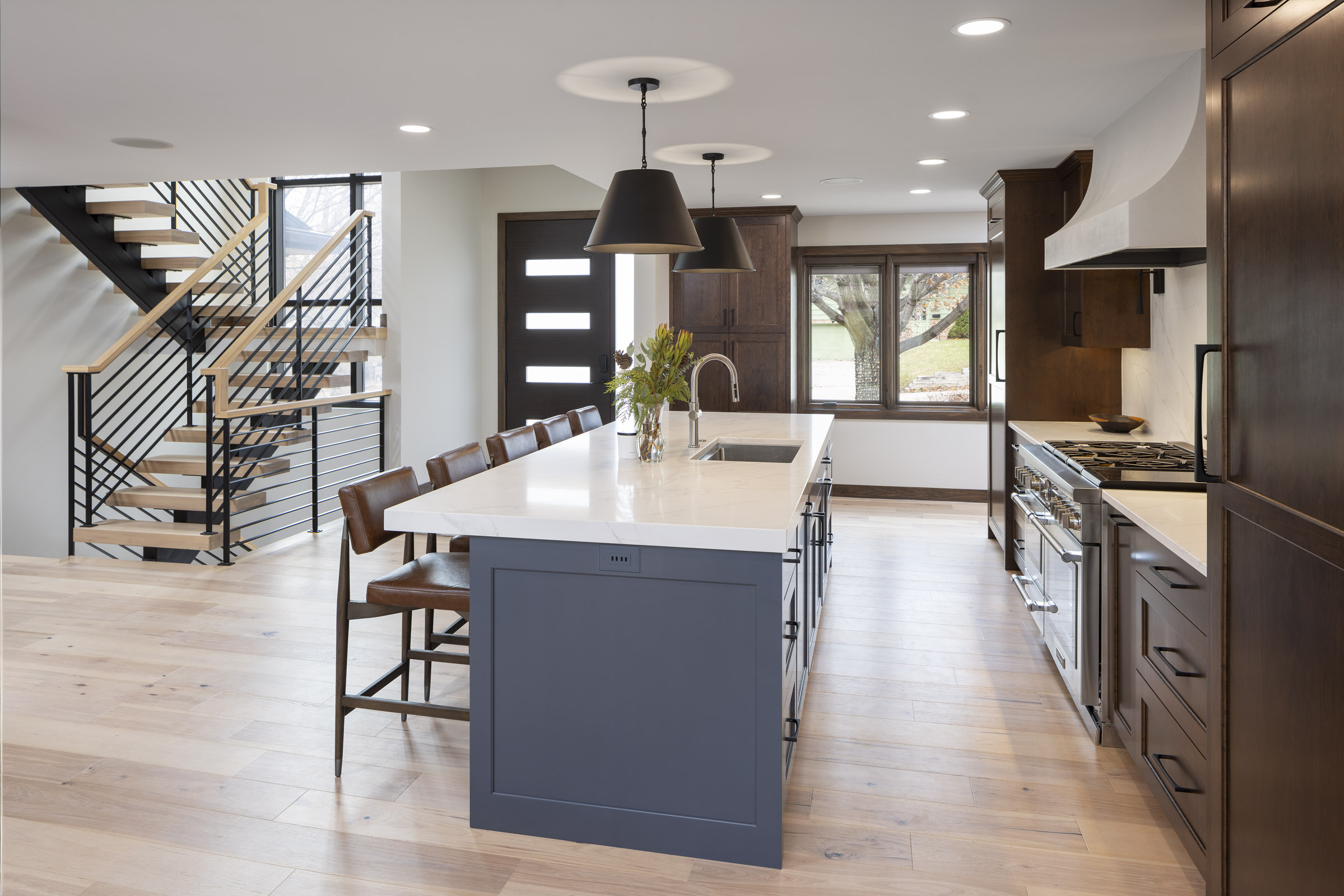 Modern open-concept kitchen featuring a large blue island with a white countertop, dark wood perimeter cabinets, and a view of a modern floating staircase. Part of a whole house remodel in Edina, MN.