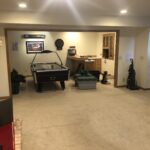 The original layout of a multi-purpose basement in Edina, featuring a large game room area with an air hockey table and a separate, open nook used as a workshop, a before photo of a basement remodel project.