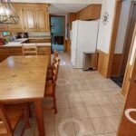 The original, dated eat-in kitchen featuring a large wood dining table, golden oak cabinets, square tile flooring, and wood wall paneling, a before photo of a kitchen remodel in Bloomington, MN.