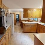 The original, dated galley-style kitchen featuring golden oak cabinets, square tile flooring, and a peninsula that creates a narrow walkway, a before photo of a kitchen remodel in Bloomington, MN.