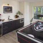 A fun and functional lower level game room, featuring a custom wet bar with dark shaker cabinets and gold hardware, and a large air hockey table ready for play, part of a lower level remodel in Edina, MN.