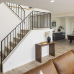 A modern open staircase with a simple black metal railing that descends into the lower level, with a view of the game room's air hockey table and wet bar in the background, part of a lower level remodel in Edina, MN.