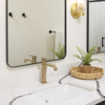 A detailed view of a modern bathroom vanity, featuring a white quartz countertop with dramatic black veining, a brushed brass faucet, and a modern brass and glass wall sconce, part of a lower level remodel in Edina, MN.