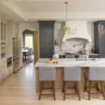 A luxurious and elegant transitional kitchen featuring a large island with a dramatic waterfall countertop, a mix of dark blue and light beige cabinets, and a custom curved range hood, part of a kitchen remodel in Inver Grove Heights, MN.