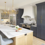 A luxurious and elegant transitional kitchen featuring a large island with a dramatic waterfall countertop, a mix of dark blue and light beige cabinets, and a custom curved range hood, part of a kitchen remodel in Inver Grove Heights, MN.