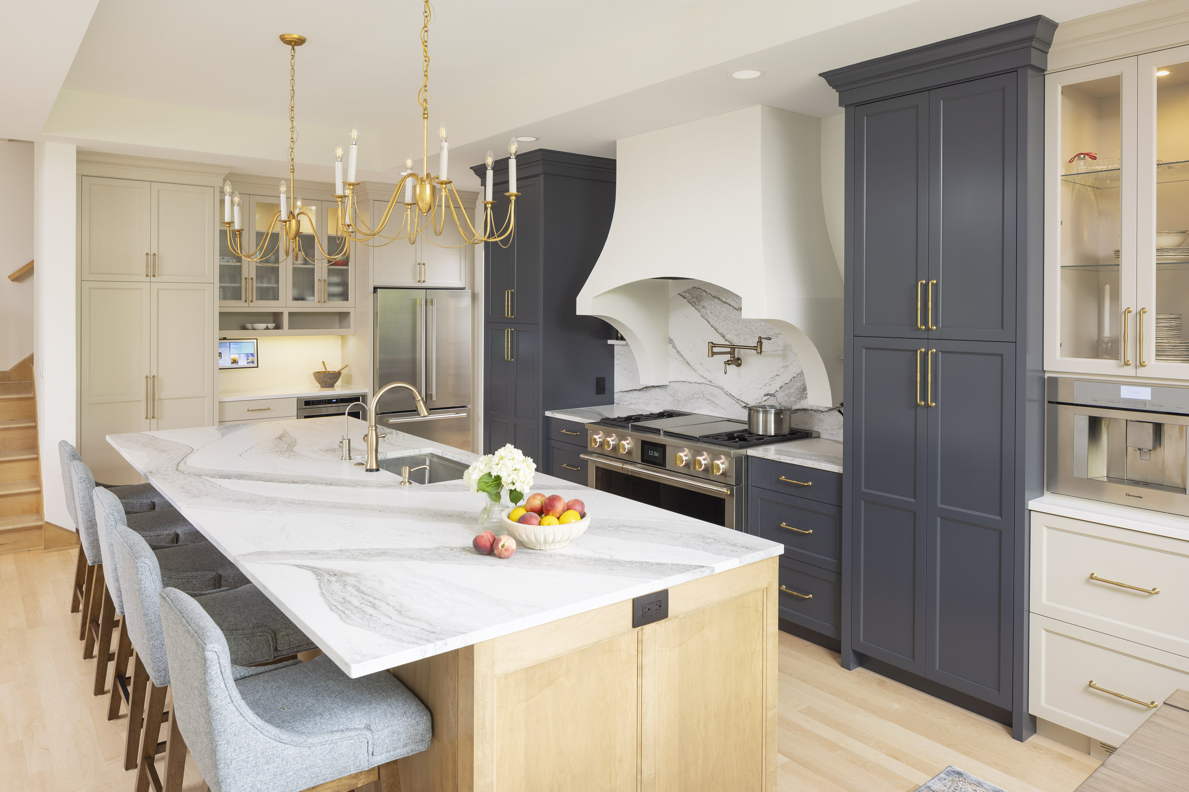 A luxurious and elegant transitional kitchen featuring a large island with a dramatic waterfall countertop, a mix of dark blue and light beige cabinets, and a custom curved range hood, part of a kitchen remodel in Inver Grove Heights, MN.