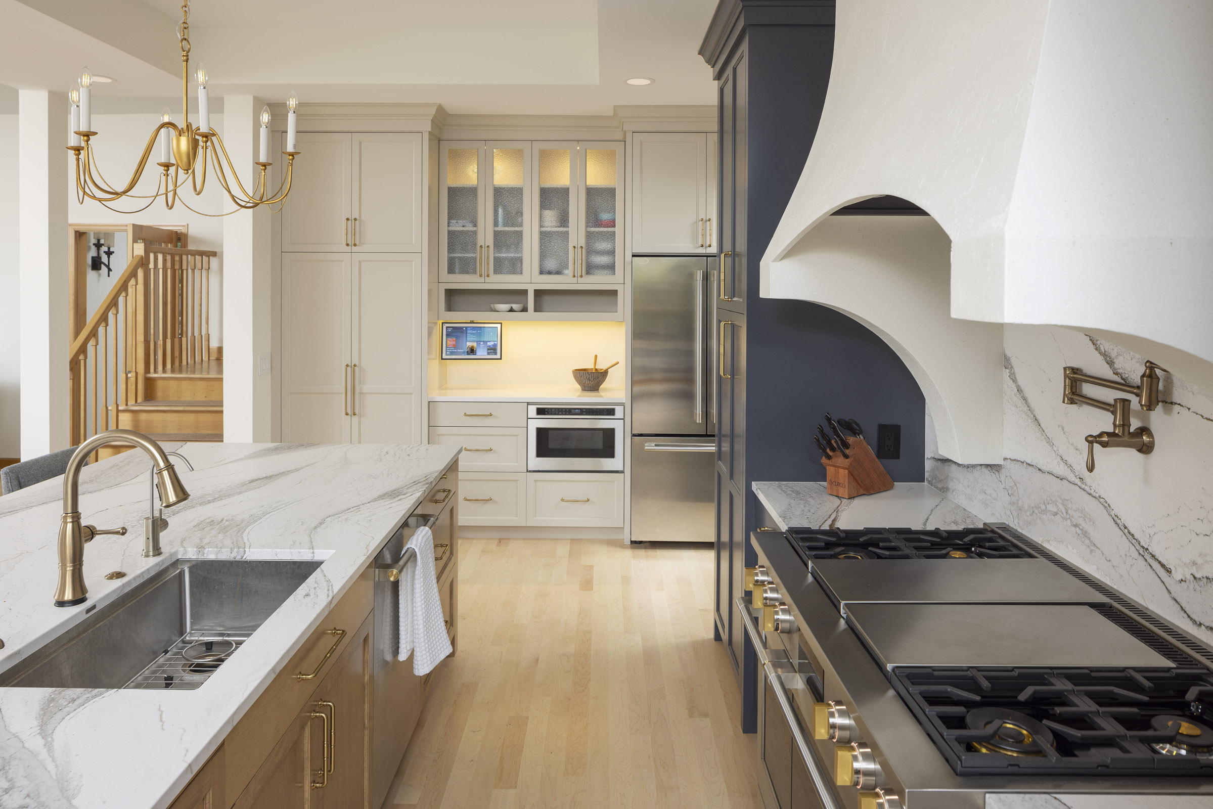 A luxurious and elegant transitional kitchen featuring a large island with a dramatic waterfall countertop, a mix of dark blue and light beige cabinets, and a custom curved range hood, part of a kitchen remodel in Inver Grove Heights, MN.