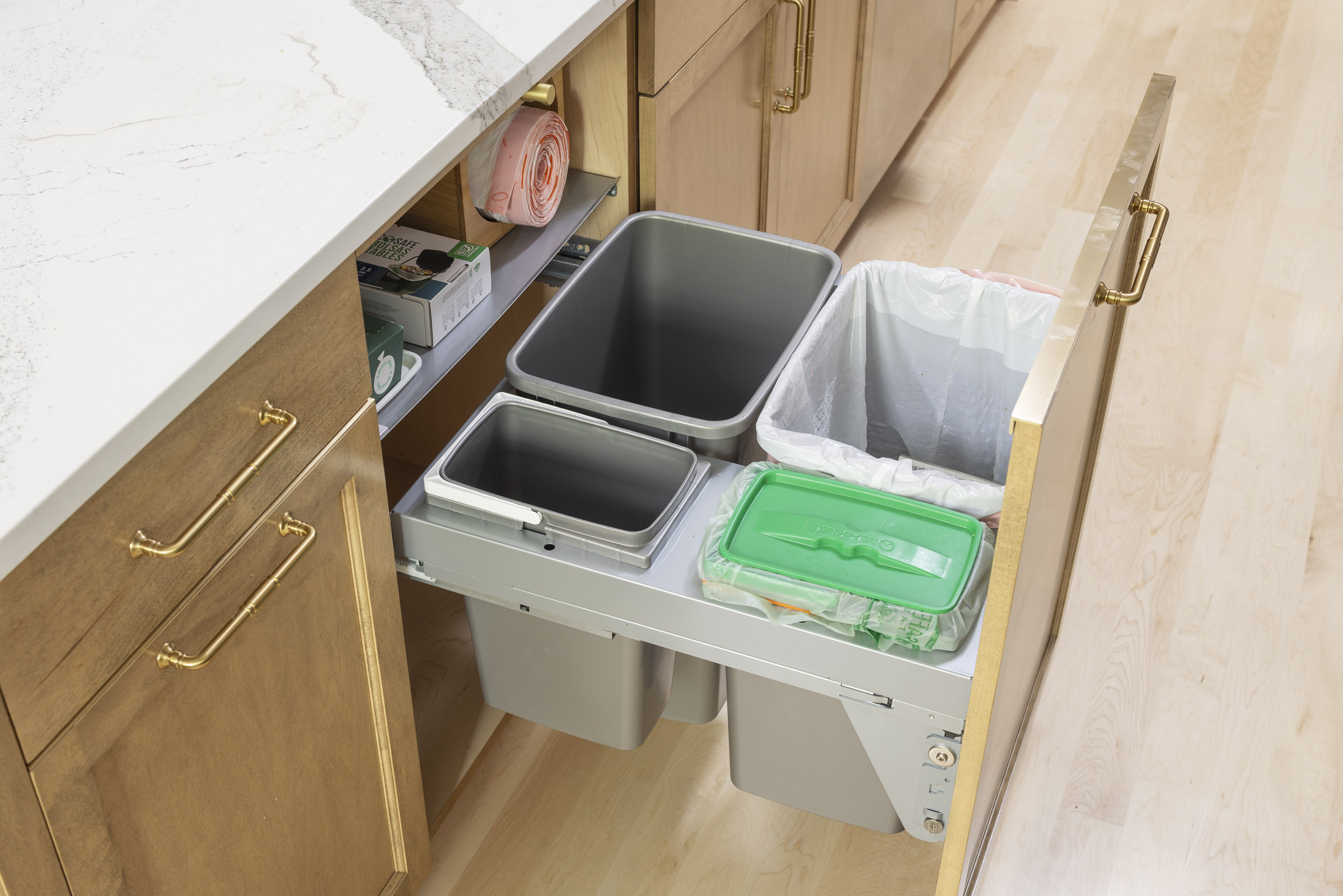 A smart and concealed kitchen waste center in Inver Grove Heights remodel, featuring a custom pull-out drawer with dedicated bins for trash, recycling, and compost, housed in a natural wood shaker cabinet, part of a kitchen remodel.