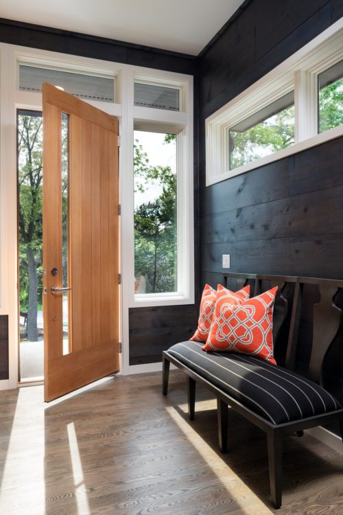 Modern front entryway featuring a light wood door and a dark accent wall made from reclaimed boards from the original home. Part of a new custom home in Chanhassen, MN.