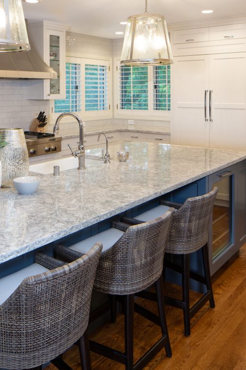 AMEK-Edina-Kitchen-Darker-2018-Cropped-21 Modern kitchen with white shaker cabinets, a large blue-grey island with a granite countertop, wicker bar stools, and stylish glass pendant lights. Part of a kitchen remodel in Edina, MN.