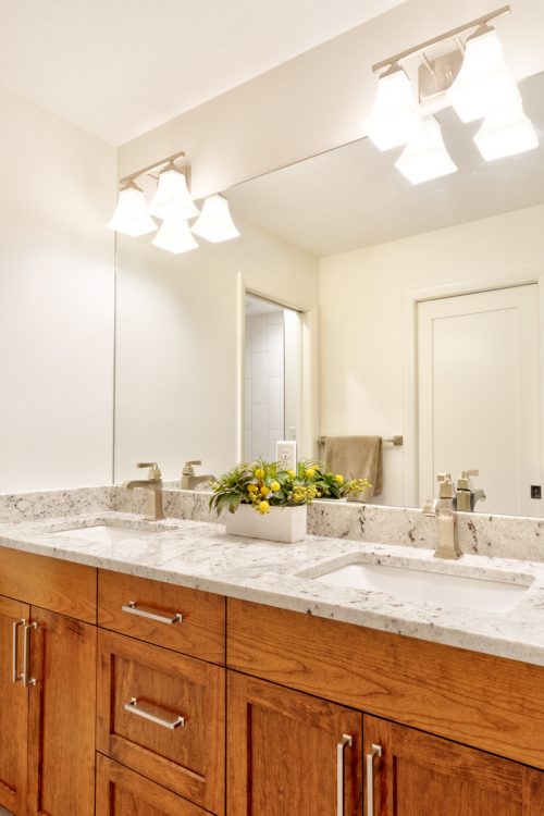 Contemporary bathroom with a long medium wood double vanity, a granite countertop, and a large wall-to-wall mirror, part of a remodel in Minnetonka, MN.